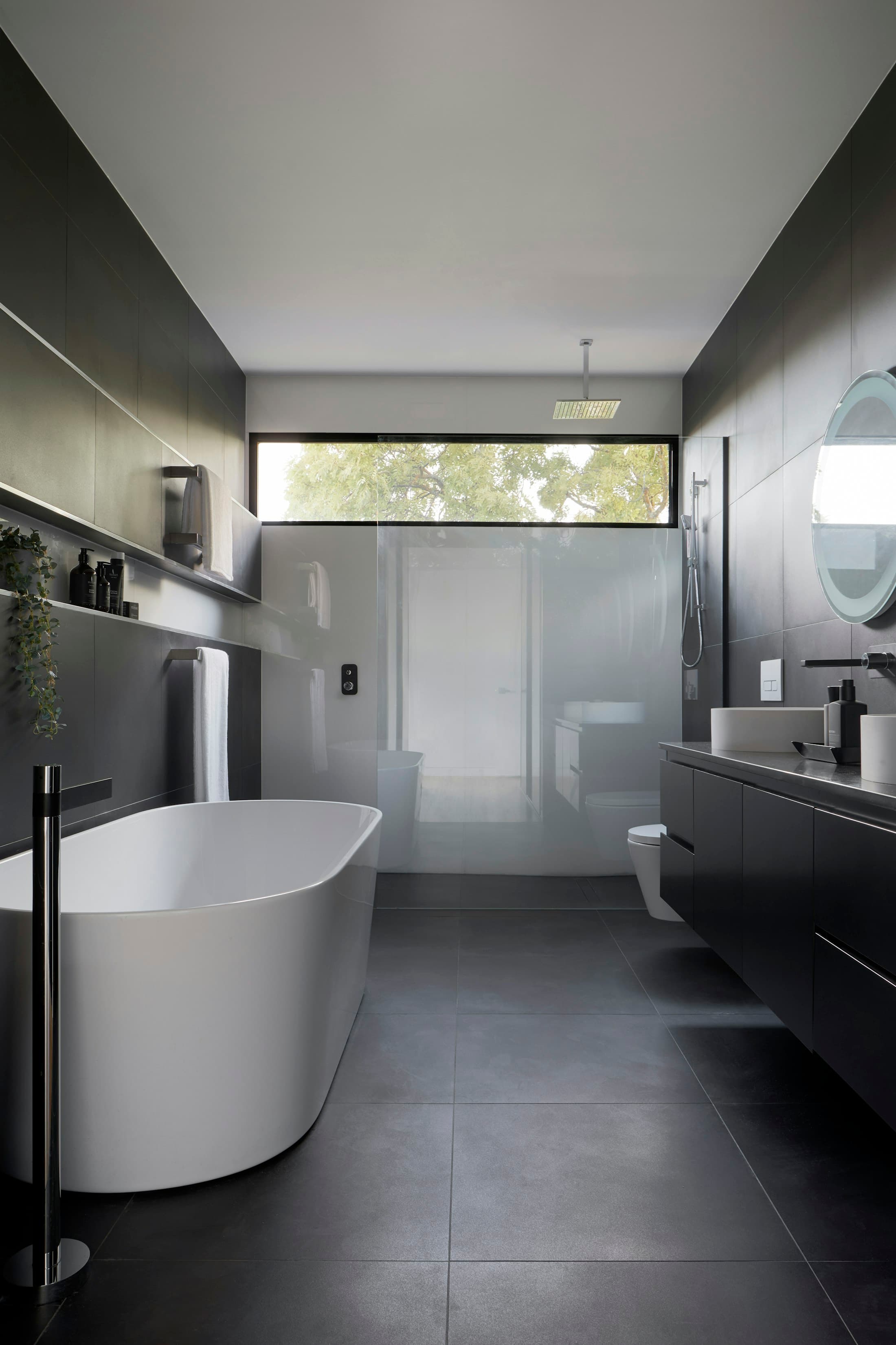 Bathroom with a freestanding bath, dark tiles and a high clerestory window