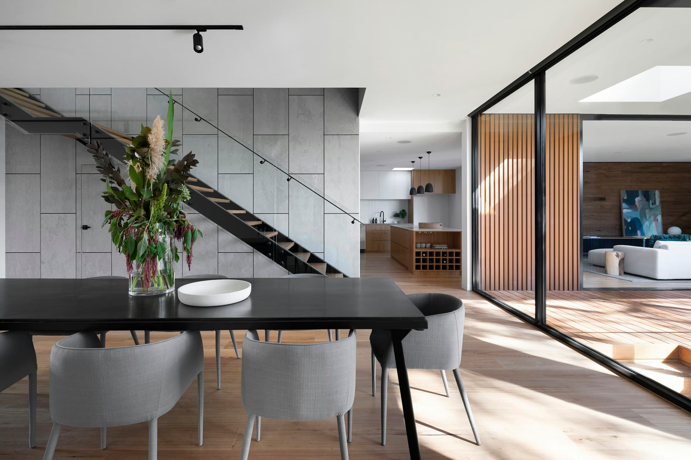 Dining area with a dark table, concrete wall, timber battens and a view through to the living room