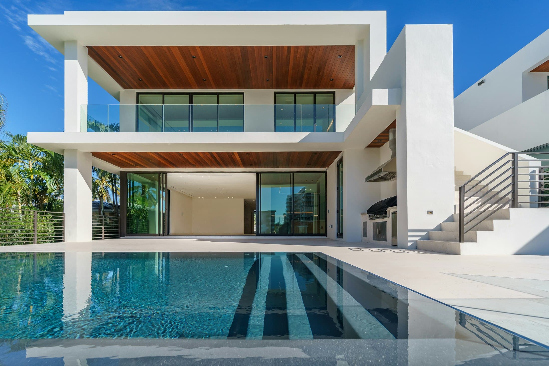 White two-storey house with a timber soffit and a long pool in the foreground