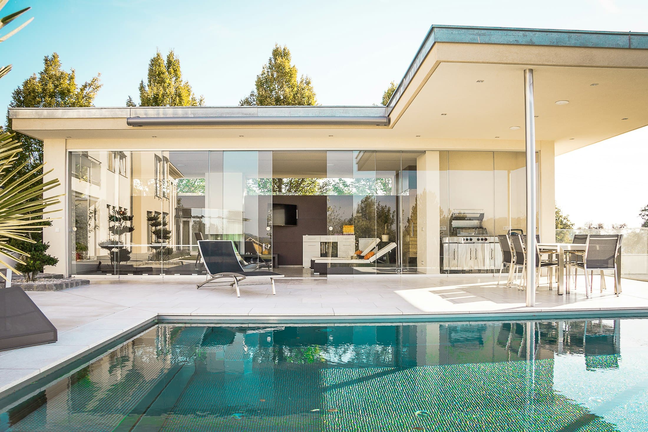 Covered terrace with sliding glass doors overlooking a pool and planting