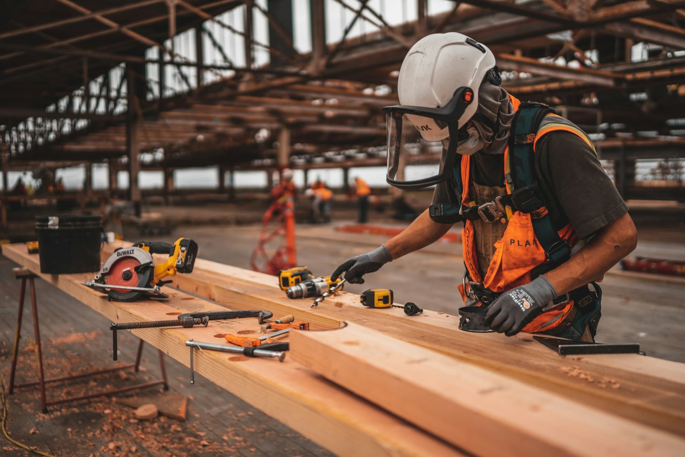 Carpenter in protective equipment measuring and cutting timber on a workshop bench