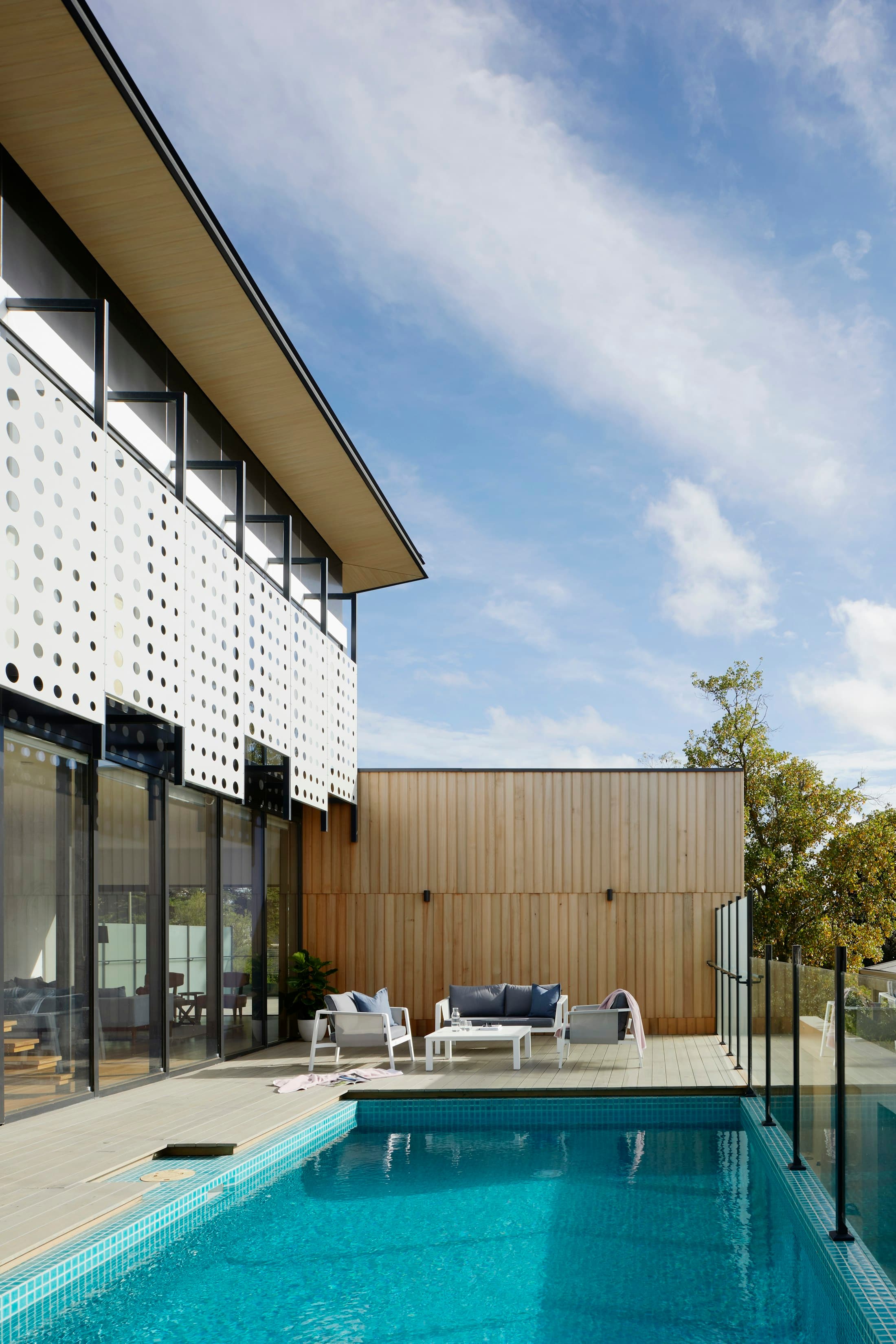 Upper-floor facade with a perforated white screen above a timber-clad ground floor