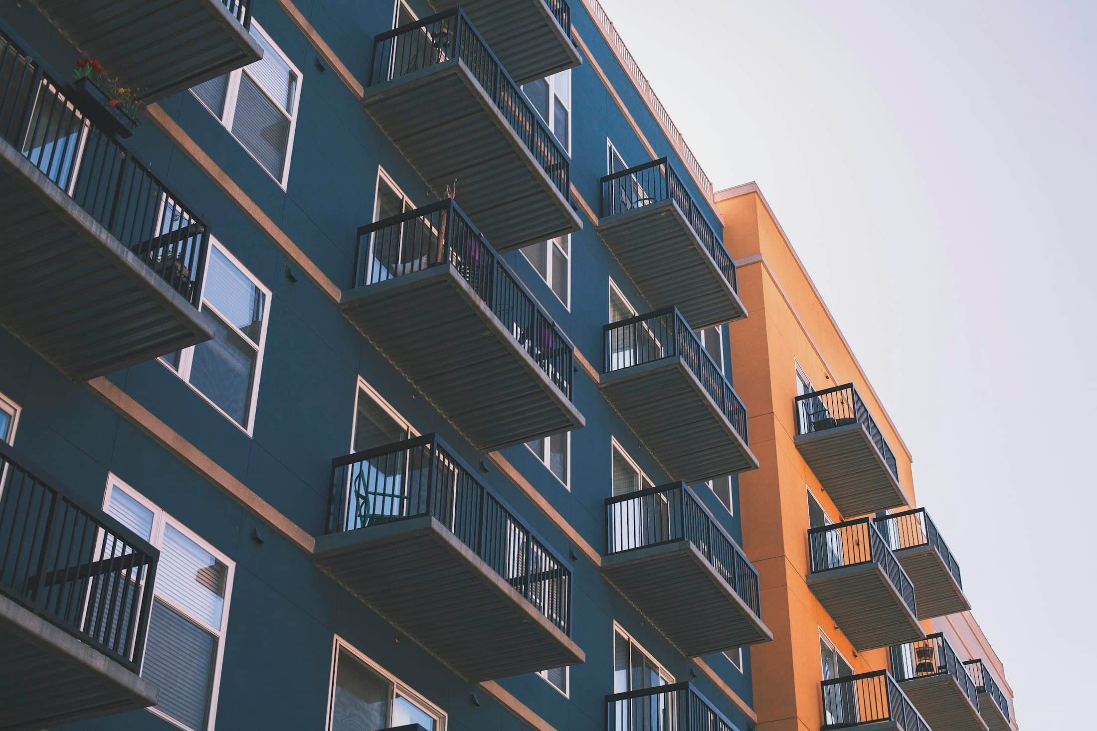 Mid-rise residential building with dark cladding, balconies and a warm orange accent wall