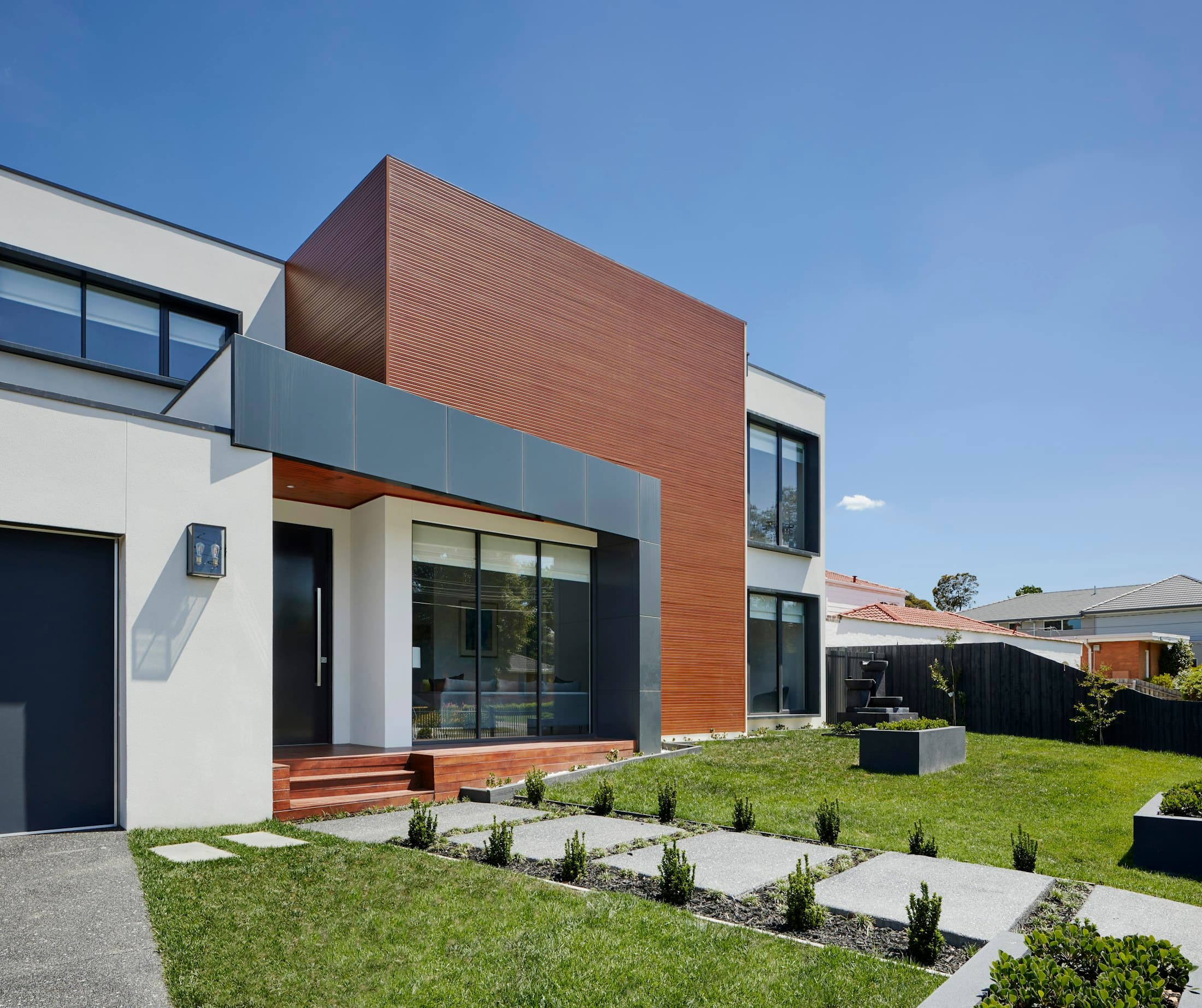 Two-storey house with a white rendered upper floor, a timber-clad volume and a new front garden