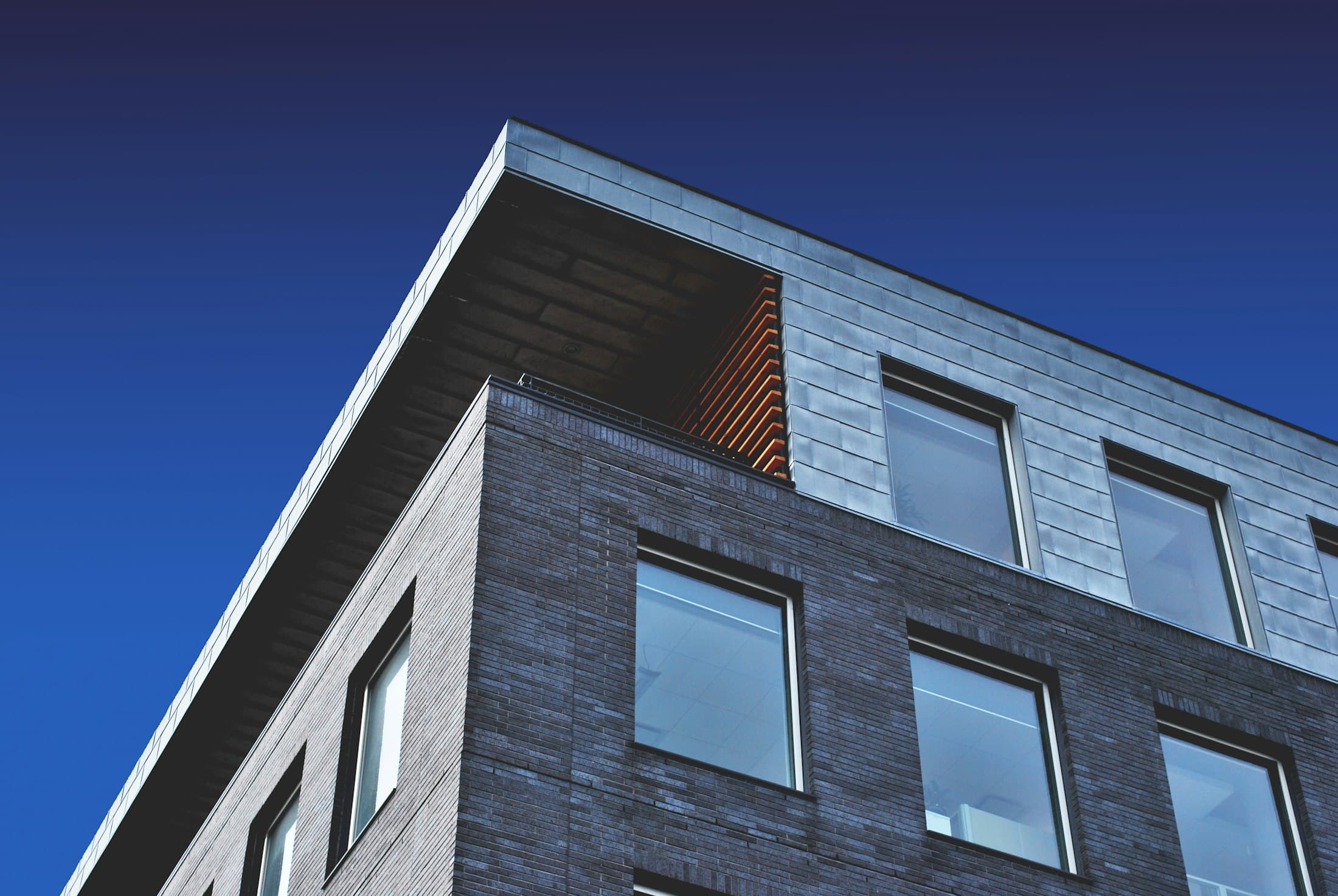 Corner of a modern commercial building with dark stone cladding and regular windows under a blue sky
