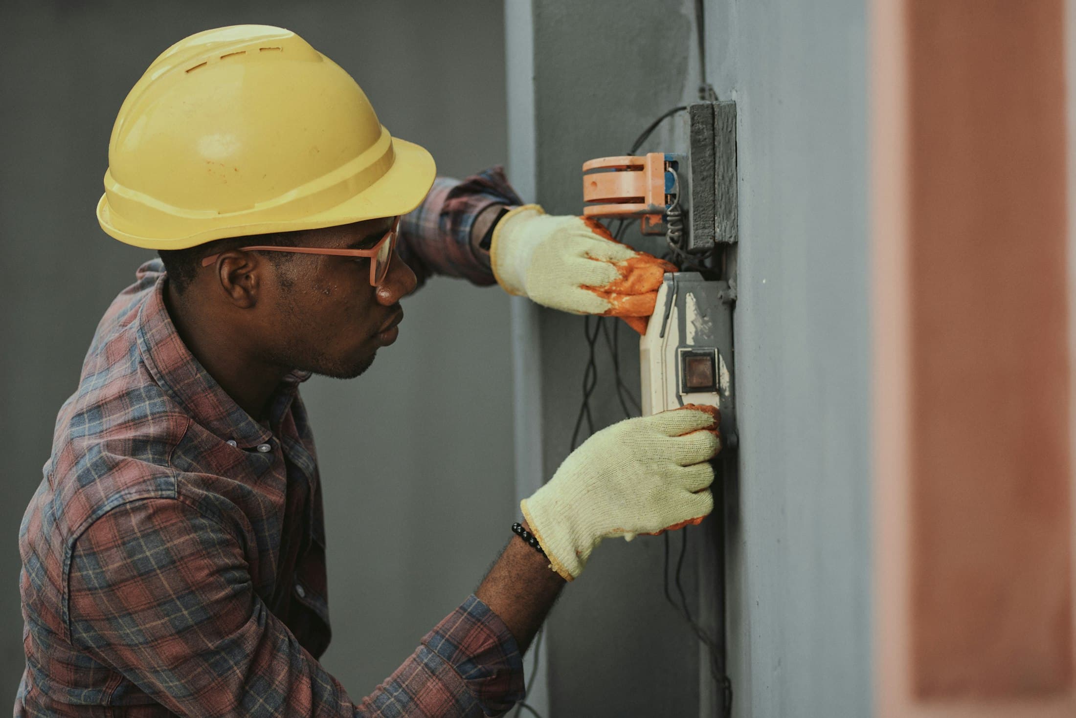 Electrician in a hard hat and gloves checking wiring at a distribution board