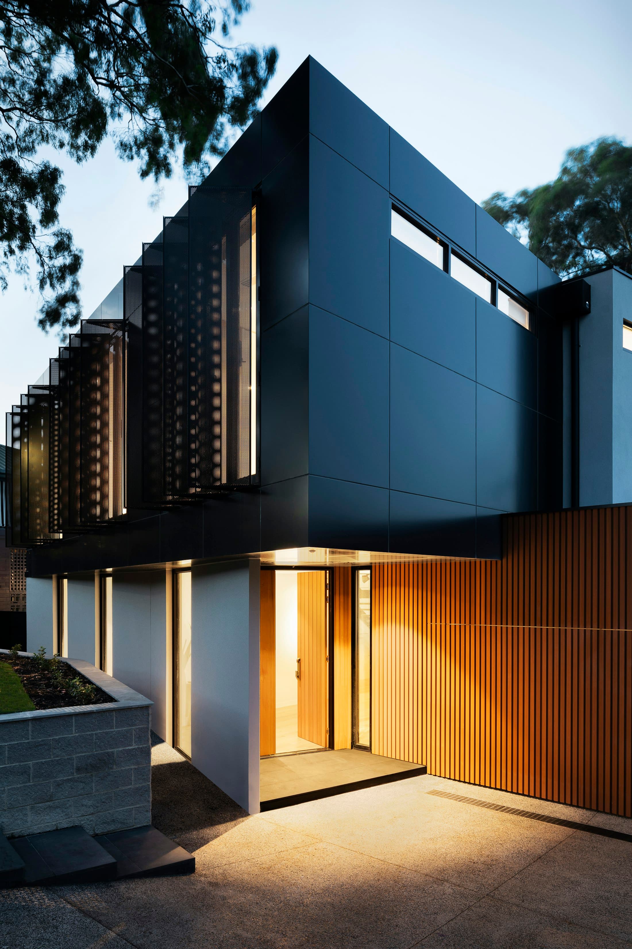 Detail of a dark facade with vertical timber battens and warm light from a recessed entrance