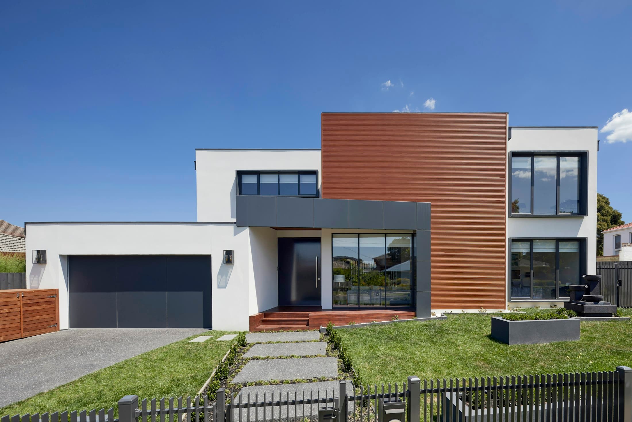 Two-storey contemporary house with white render, timber cladding and a landscaped front garden
