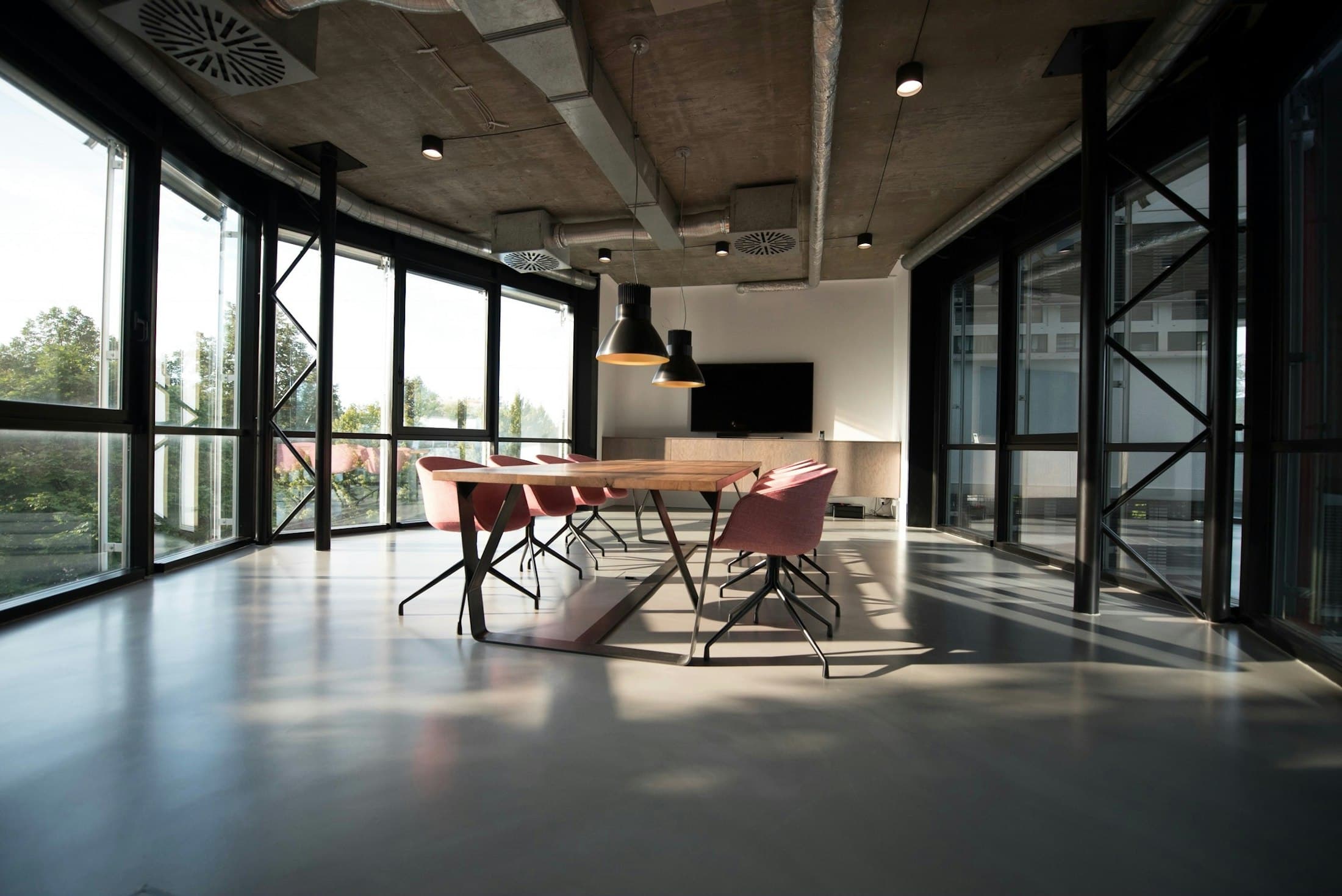 Open workspace with glazed walls, a long table and a concrete ceiling with exposed services